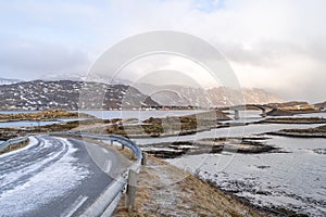 A long Atlantic Ocean winter Road and curved concrete bridge and water crossing from island in Lofoten.