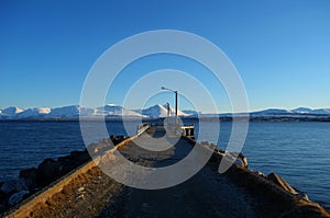 Long beautiful pier with snowy mountain and blue fjord