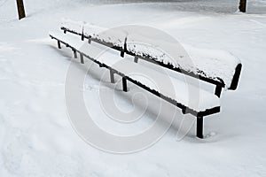 Long black metal sports spectator bench covered in snow on a snowy field