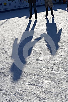 Long blue shadows on the ice at the ice rink from a group of skaters. Winter sunny day. Outdoor activities concept.