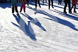 Long blue shadows on the ice at the ice rink from a group of skaters. Winter sunny day. Outdoor activities concept.