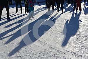 Long blue shadows on the ice at the ice rink from a group of skaters. Winter sunny day. Outdoor activities concept.