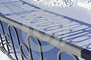 Long blue shadows on the white snow from the metal wrought iron fence on a sunny winter day. Abstraction. Background.