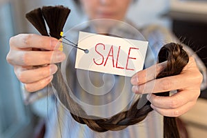 Long brown cut braid with tag in female hands, sale of woman cut hair