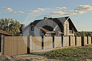 long brown fence wall made of metal and stones with a large gate in front of a gray private house