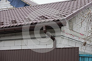 Long brown plastic drain pipe on a white brick wall of a house