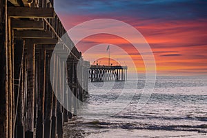 A long brown wooden pier with American flags flying on curved light posts with powerful red clouds at sunset
