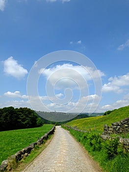 Long cobbled stone stone road running downhill in beautiful yorkshire dales countryside with green summer meadows