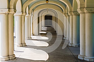 A long corridor in classical architectural style with many elegant columns and arches leading in perspective to a door