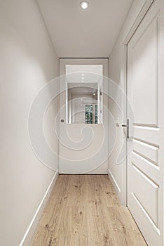 A long corridor of a house with a light wooden floor with access doors to the rooms