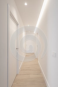 A long corridor in a house with smooth white materials and light oak flooring