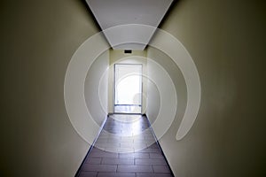 A long corridor with an open door. A bright light shines from the open door