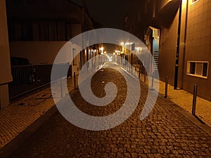 Long, dark cobbled Portuguese street at night in northern Portugal. Lit by yellow street lamps.