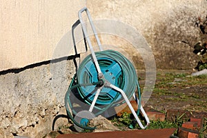 Long dark green garden hose mounted on garden hose reel with small wheels for easier transfer left in family house backyard
