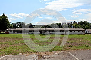 Long dilapidated military hangars with broken windows and destroyed walls surrounded with grass and family houses