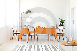 Long dining room table covered with orange tablecloth and comfortable white chairs