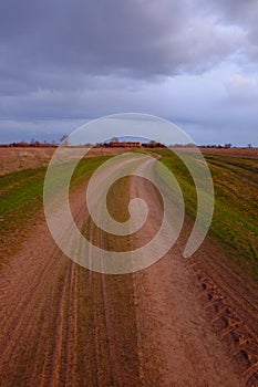 Long dirt road in the fields. Cloudy evening landscape