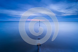 Long dock stretching into the ocean at twilight, with cloudy skies in the backdrop