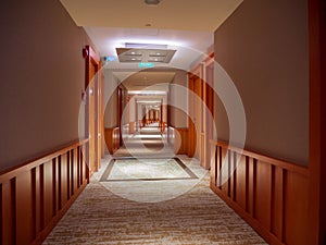 Long empty carpeted hallway / corridor in the interior of a hotel flanked by wooden doors