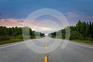 long empty road surrounded by trees and a dramatic sky