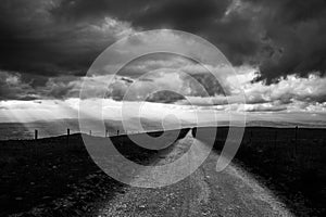 A long, endless mountain road beneath a moody sky with distant sunrays