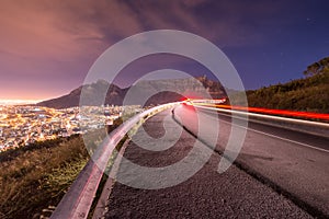 Long exposure of car driving around a bend with Table Mountain in the background in Cape Town as seen from Signal hill.
