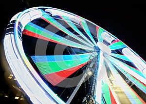 Long exposure motion blur of a spinning ferris wheel at night illuminated in bright neon colors