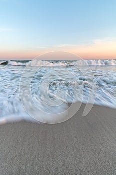 Long exposure of the movement of waves crashing on a sandy beach. Pastel sunset colors