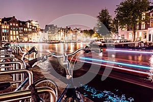 Long Exposure Night city view of Amsterdam with Light trails of Boat in channel and typical dutch houses on background