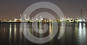 Long exposure night photo crude oil refinery plant and many chimney with petrochemical tanker or cargo ship at coast of the river