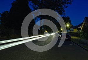 Long exposure of a nocturnal side street with lit lanterns, star-shaped halos and a line-shaped light trail of a passing car