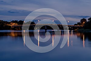 Long exposure photograph of old railway bridge over river at night with reflection in Ratchaburi Thailand