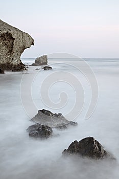 Long exposure photograph, with a rock formation in the foreground and a cliff in the background.