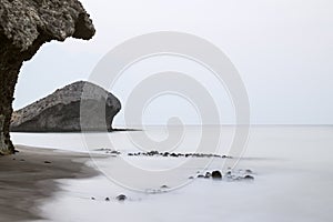 Long exposure photograph, with a rock formation in the foreground and a cliff in the background.