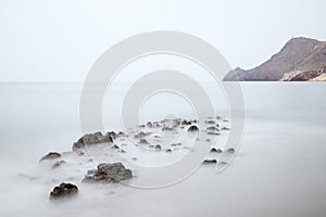 Long exposure photograph, with a rock formation in the foreground and a cliff in the background.