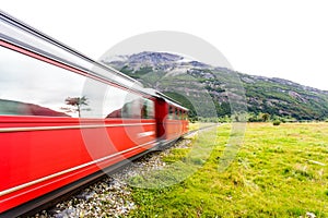 Long exposure of red train riding along green grassy field