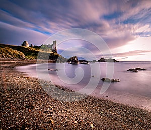 Long exposure of seascape featuring the old vintage ruins of Dunure Castle with wispy smooth clouds and ocean