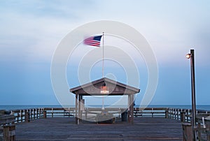 A long exposure of a shelter at the end of a pier with an American flag.