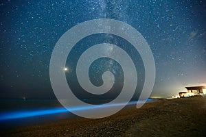 Long exposure shot of glowing plankton on sea surf and milky way. Blue bioluminescent glow of water under the starry sky