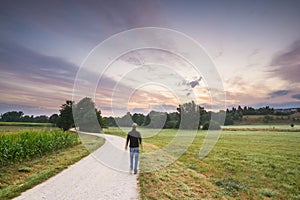 Long exposure shot of a man walking a dirt road towards a sunset - path to happiness concept