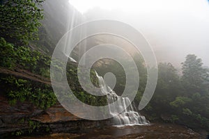 Long exposure shot of a scenic waterfall and white dark forest on a foggy day, Katoomba Falls