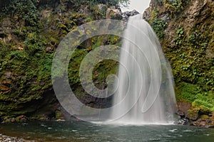 Long exposure shot of a waterfall flowing through a missy rough cliff in Xico, Veracruz, Mexico