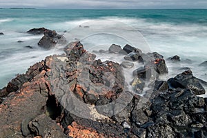 Long exposure with some red crabs resting on the volcanic rocks of a beach. Isabela Island, Galapagos