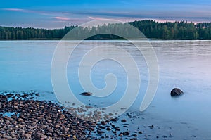 Long Exposure of Sunset at the Paijanne lake. Beautiful scape with stone beach, pine forest and water. Lake Paijanne