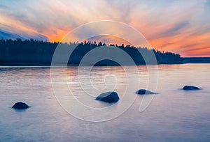 Long Exposure of Sunset at the Paijanne lake. Beautiful scape with stone beach, pine forest and water. Lake Paijanne, Finland