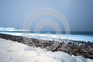 Long exposure of the surf breaking over stone boulders on a snow covered beach