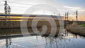 Long exposure train with setting sun shining through the train on Dutch traintrack.