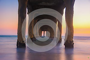 Long exposure underneath the Manhattan beach Pier on the coast of the Pacific Ocean at sunset