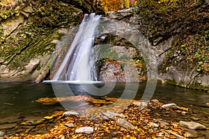 Long exposure view of the beautiful Pruncea Casoca Waterfall with fallen leaves in an autumn landscape