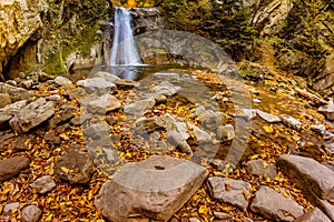 Long exposure view of the beautiful Pruncea CaÅŸoca Waterfall with fallen leaves in an autumn landscape